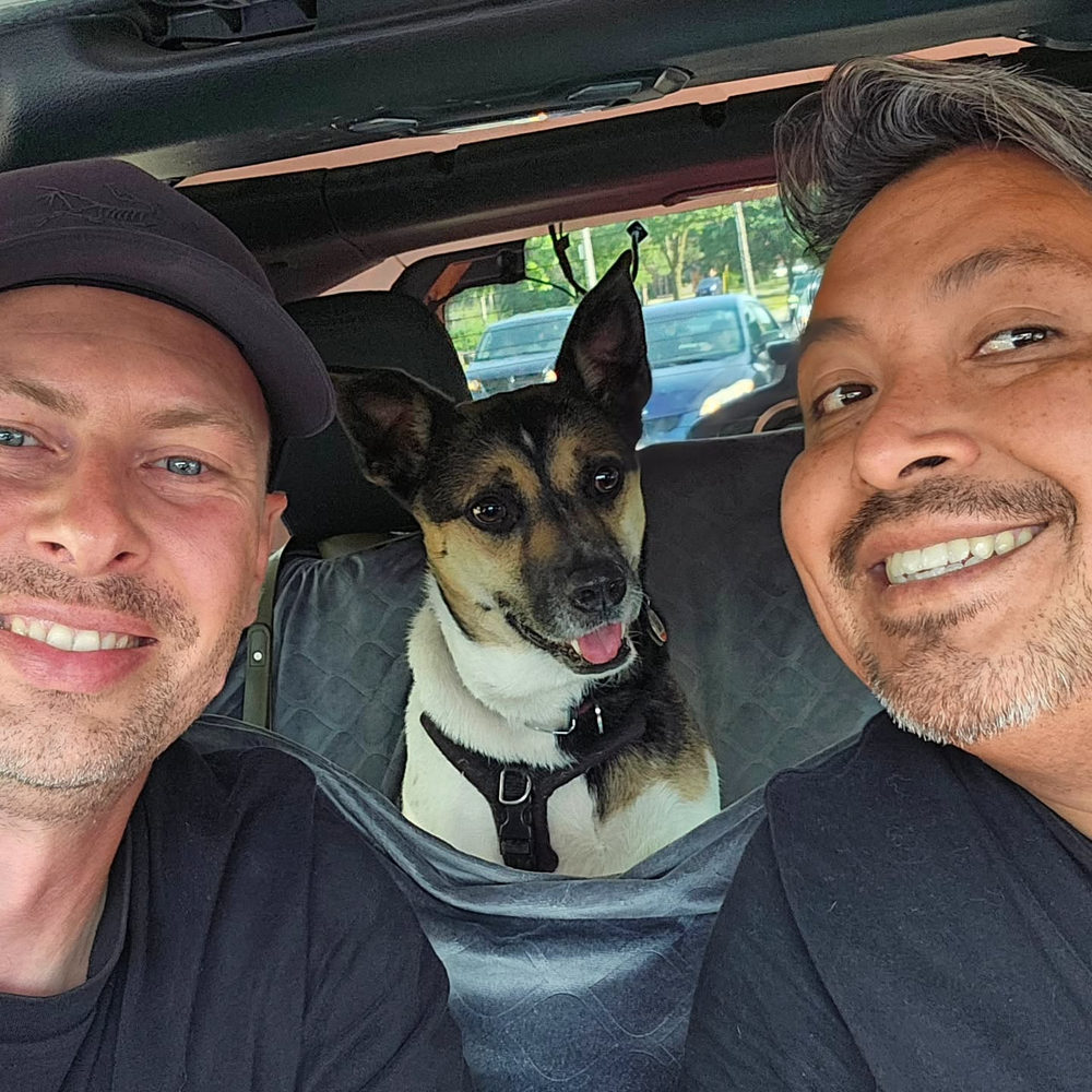 Abraham and Max smiling in the front seats of the Jeep with a dog between them